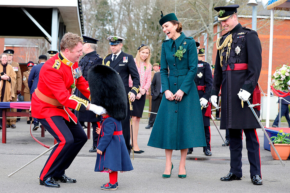 Кэтрин, герцогиня Кембриджская, и принц Уильям, герцог Кембриджский смеются, когда подполковник Роб Мани надевает медвежью шапку на голову своей дочери Гайи Мани во время Парада в честь Дня Святого Патрика в казармах Монс 17 марта 2022 года в Олдершоте, Англия
