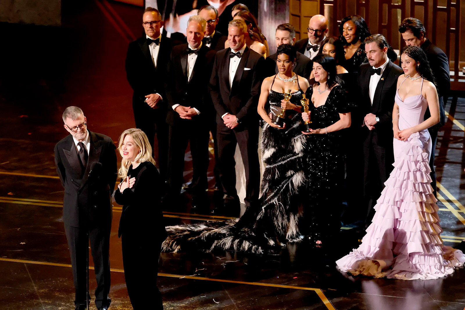 Пол Томас Андерсон, Сара Мерфи, Энтони Карлино, Уилл Вайске, Энди Юргенсен, Тейана Тейлор, Майкл Бауман, Кассандра Кулукундис, Реджина Холл, Шейна Макхейл, известная как Junglepussy, Леонардо Ди Каприо, Чейз Инфинити и Бенисио дель Торо принимают награду за лучший фильм «Одна битва за другой» на сцене во время 98-й церемонии вручения премии «Оскар» в театре Dolby 15 марта 2026 года в Голливуде, Калифорния.