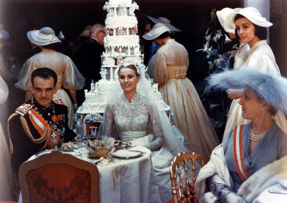 Принц Монако Ренье III и его супруга принцесса Грейс на приёме, который последовал за свадебной церемонией 18 апреля 1956 года. На заднем плане королевских молодожёнов &ndash; семиярусный торт, увенчанный короной Монако