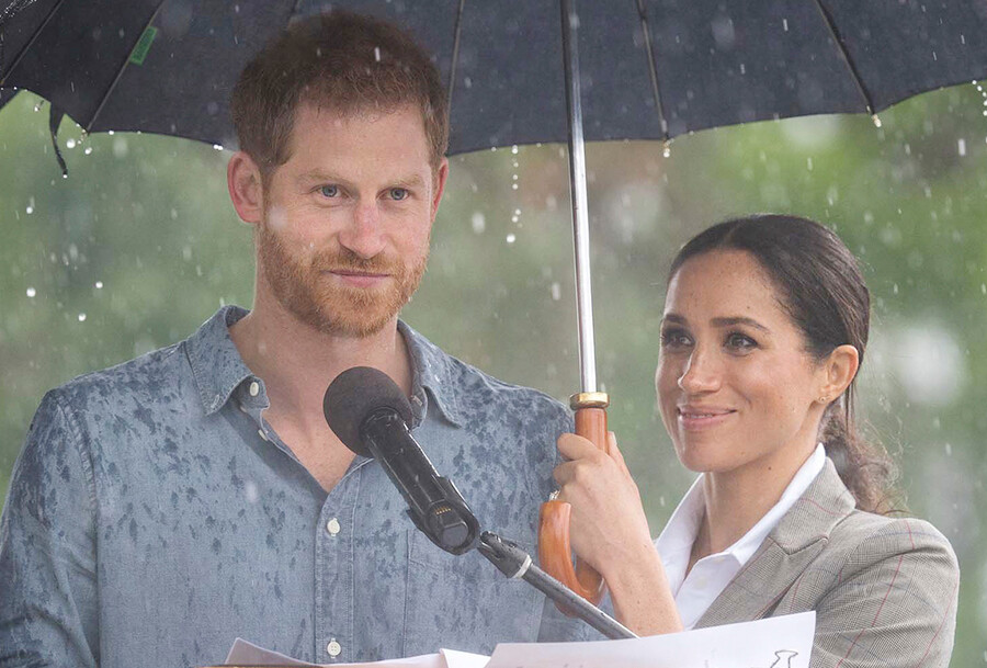 Принц Гарри выступает на трибуне под дождем Меган держит зонтик 