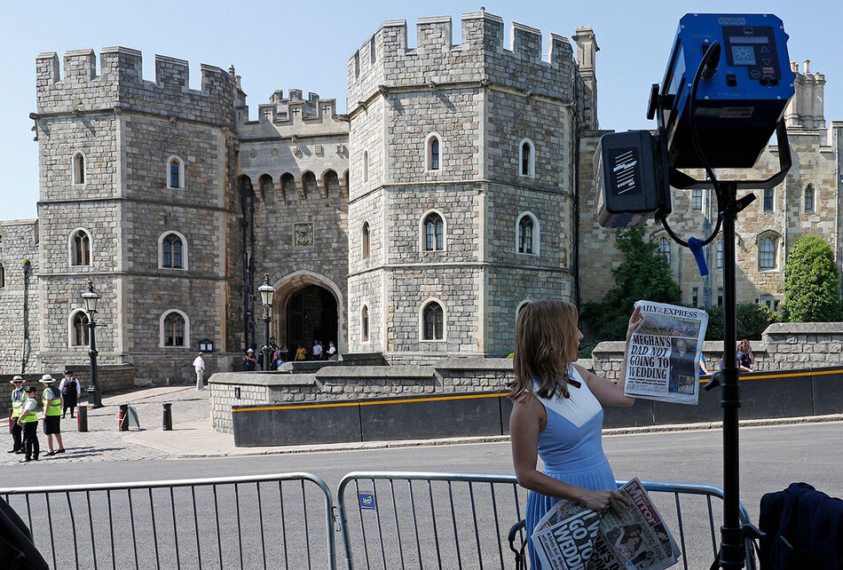 Тележурналист CNN держит британскую газету, в которых рассказывается история отца Меган Маркл Томаса Маркла, напротив ворот Генриха VII Виндзорского замка в Виндзоре, к западу от Лондона, 15 мая 2018
