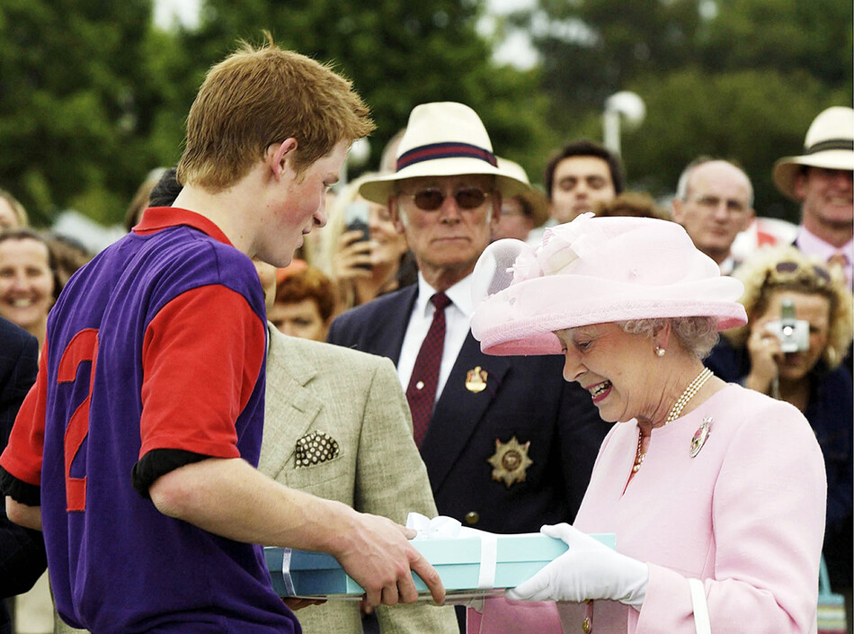 Королева Елизавета II делает подарок принцу Гарри после матча по поло во время королевского Аскот 18 июня 2003 года в Виндзоре, Англия