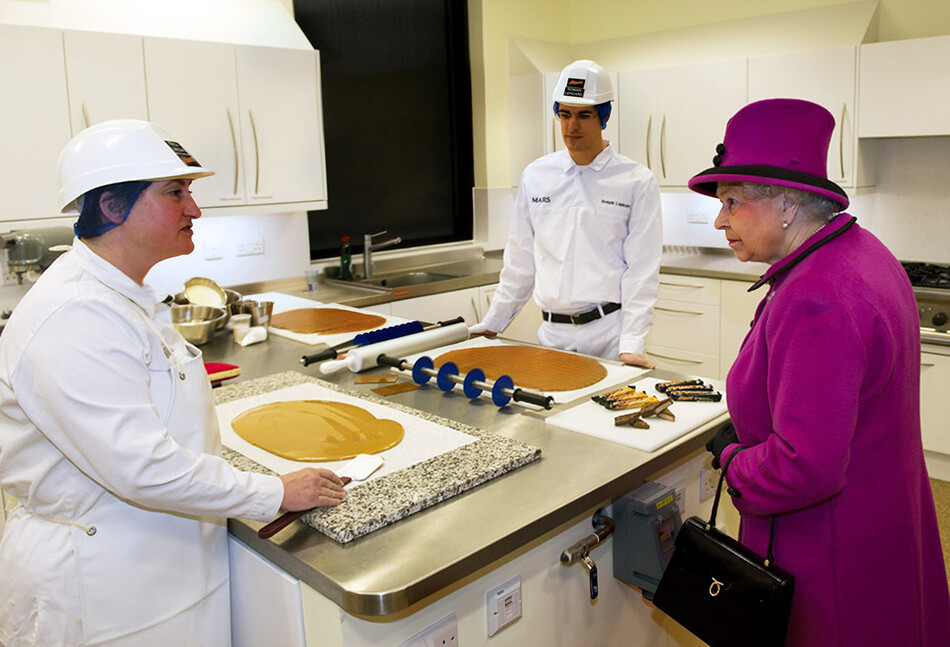 Королева Великобритании Елизавета II (справа) беседует с учёными-инноваторами Паулой Линегар (слева) и Роменом Лепикардом (справа) во время визита на фабрику по производству шоколадных батончиков Mars Chocolate UK в Слау, южная Англия, 5 апреля 2013