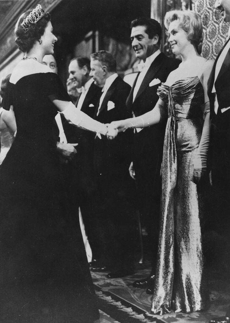 Королева Елизавета II протягивает руку Мэрилин Монро во время визита королевы со знаменитостями на Королевском киноспектакле.&nbsp;Рядом с Мэрилин стоит актёр Виктор Мэтьюр, 1956