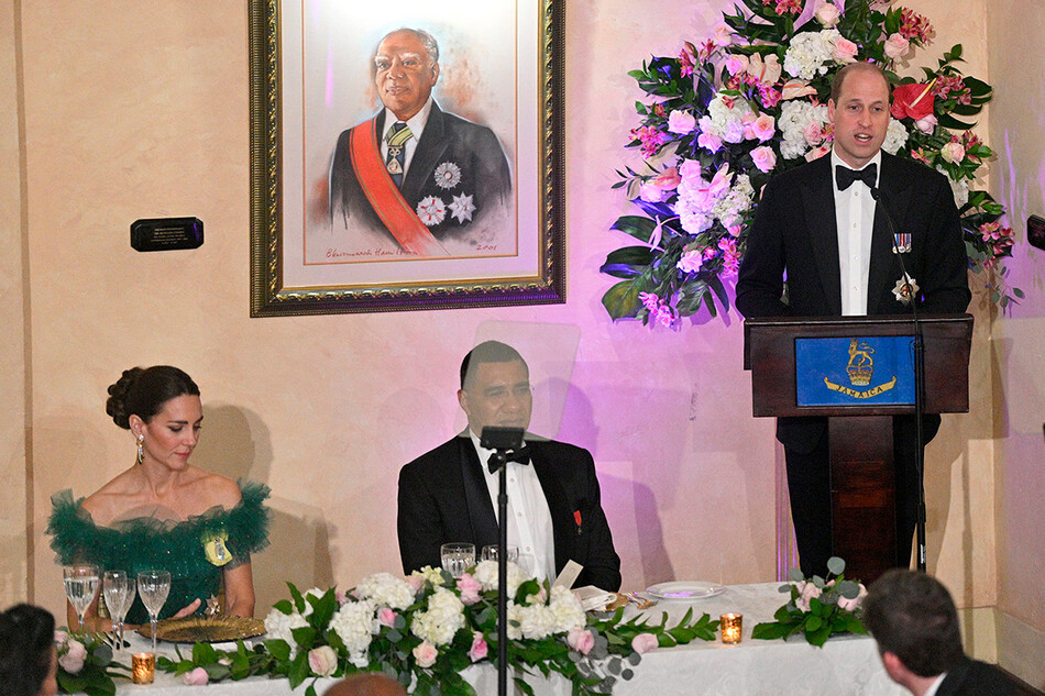 Кэтрин, герцогиня Кембриджская и премьер-министр Ямайки Эндрю Холнесс смотрят, как принц Уильям, герцог Кембриджский, выступает на сцене во время ужина, устроенного генерал-губернатором Ямайки в Королевском доме 23 марта 2022 года в Кингстоне, Ямайка