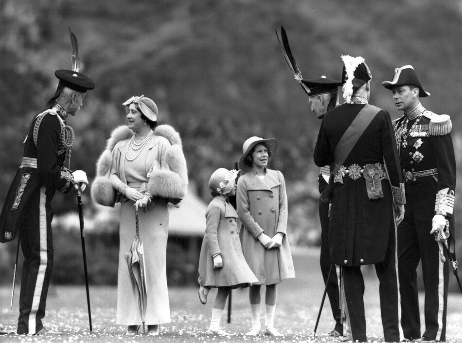 Королева Елизавета разговаривает с лордом Эльфинстоном во время инспекции Королевской роты лучников во дворце Холирудхаус в Эдинбурге. Её муж король Георг VI (1895 - 1952) - справа; Принцессы Елизавета и Маргарет Роуз (1930-2002) в центре