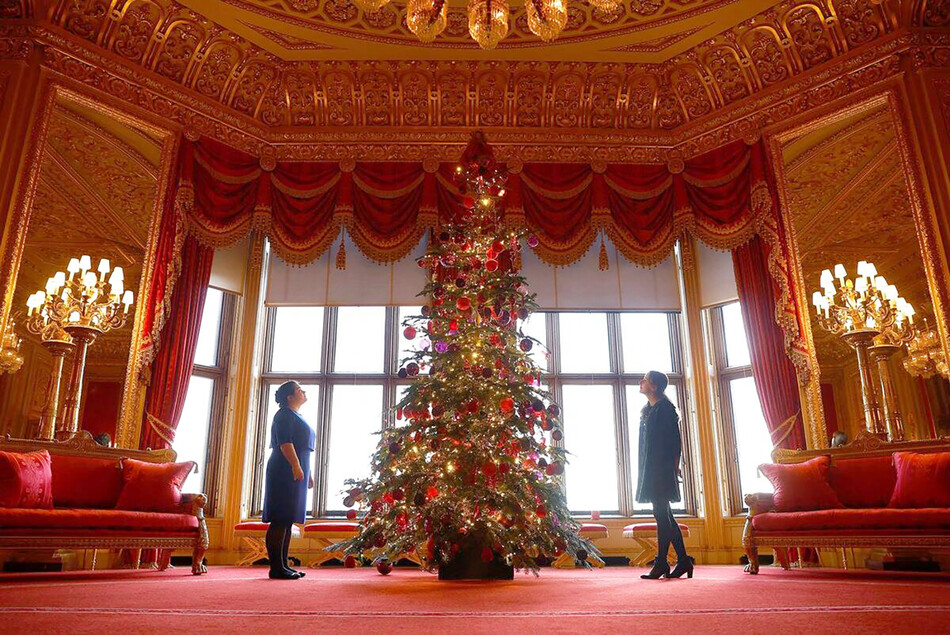Сотрудники фонда Royal Collection Trust позируют фотографу у недавно установленной и украшенной рождественской ёлки в Багровой гостиной в Виндзорском замке, 2022г.