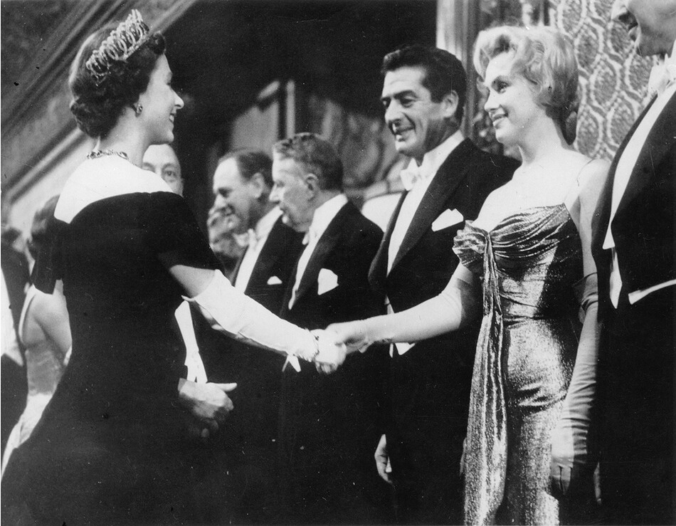 Королева Елизавета II протягивает руку Мэрилин Монро во время визита королевы со знаменитостями на Королевском киноспектакле.&nbsp;Рядом с Мэрилин стоит актёр Виктор Мэтьюр, 1956