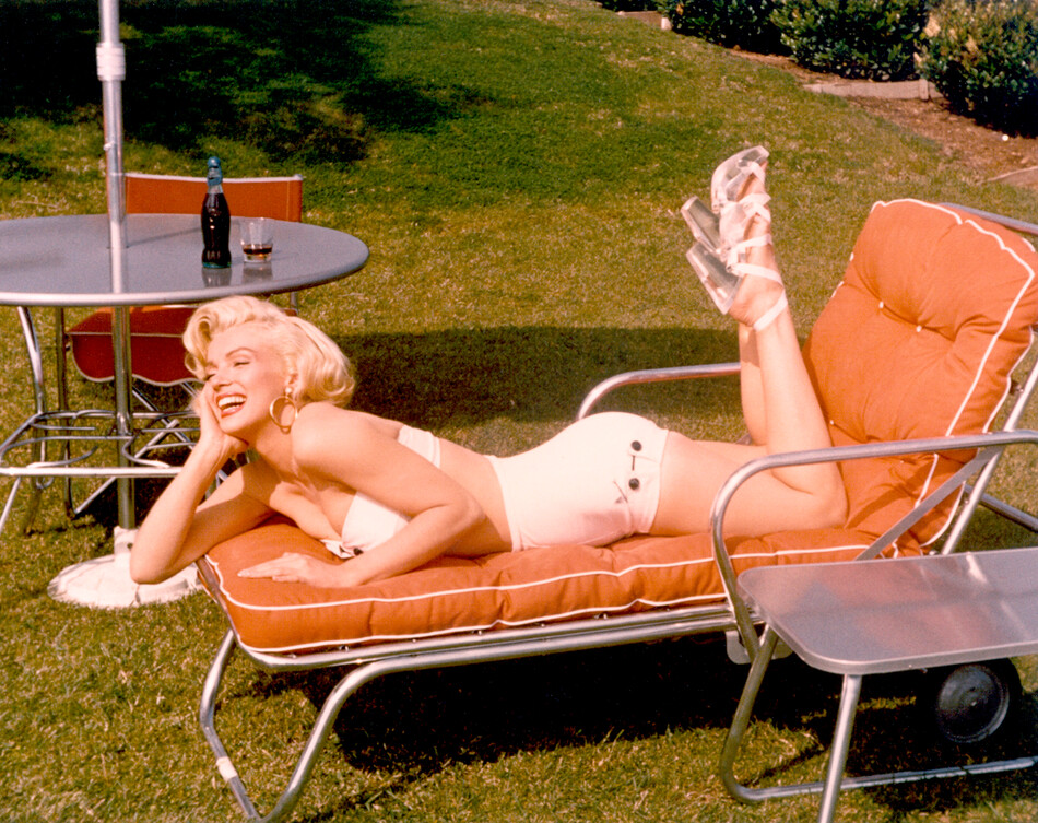 Мэрилин Монро позирует для портрета в купальном костюме и на высоких каблуках с бутылкой кока-колы в стакане на столе позади нее, примерно 1953 год