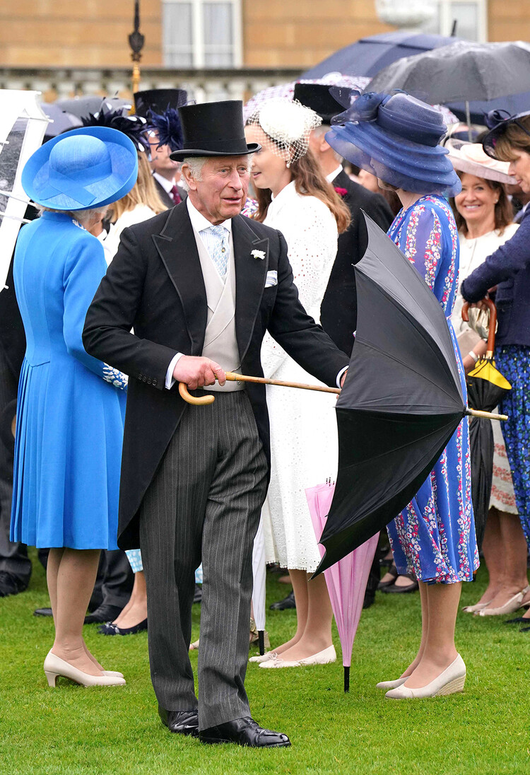 Принц Чарльз, принц Уэльский, закрывает зонт на вечеринке в Королевском саду в Букингемском дворце в Лондоне, 11 мая 2022 года.