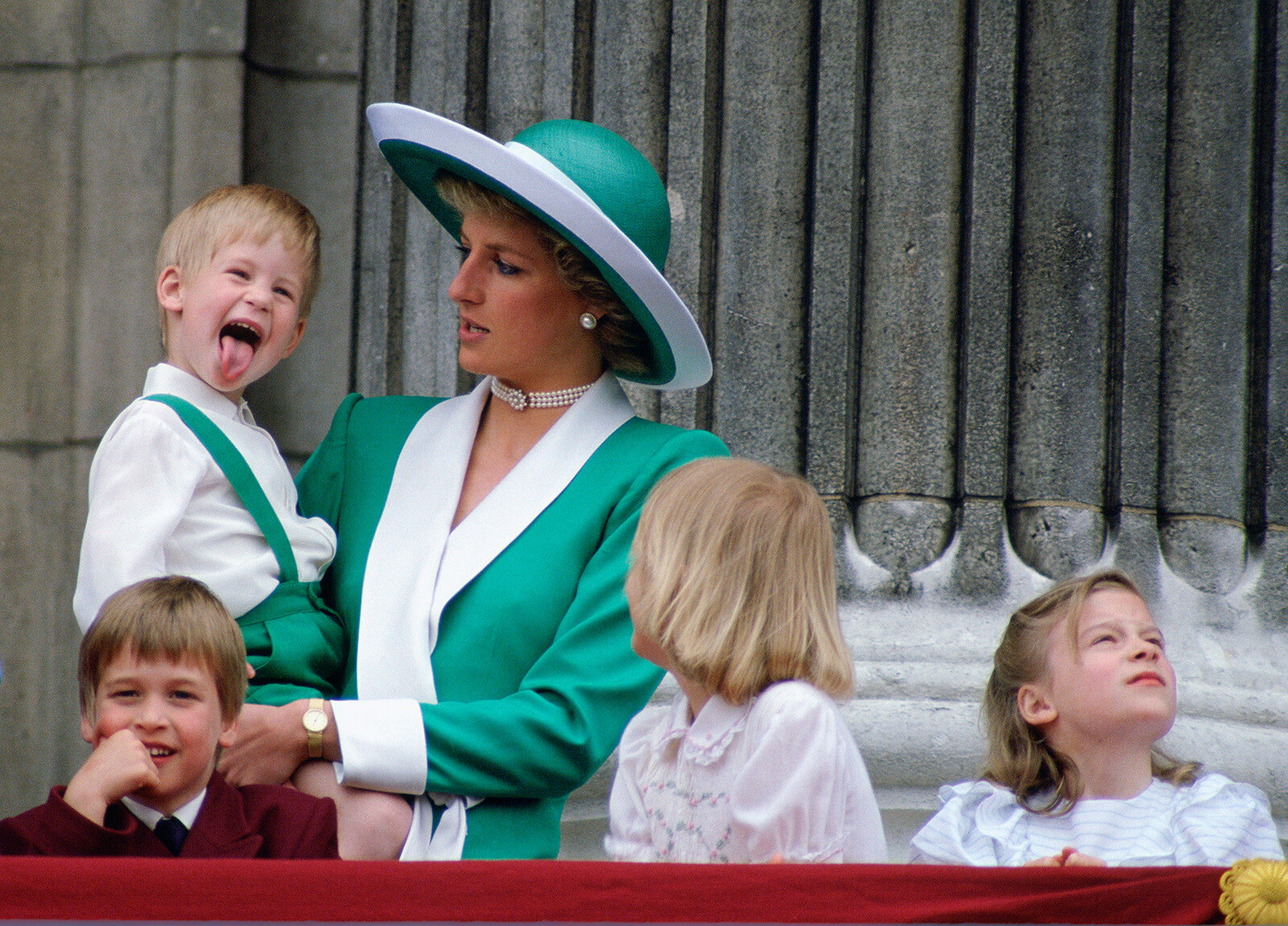 Принц Гарри высунул язык к большому удивлению своей матери, принцессы Дианы, выставившей цвет с принцем Уильямом, леди Габриэллой Виндзор и леди Роуз Виндзор, наблюдающими с балкона Букингемского дворца за&nbsp;парадом Trooping the Colour, 1988