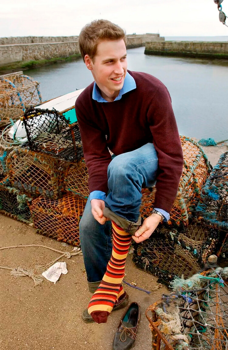 Принц Уильям натягивает носки и обувь после прогулки по песчаному пляжу возле дома своего университета 29 мая 2003 г. в Сент-Эндрюс в Шотландии