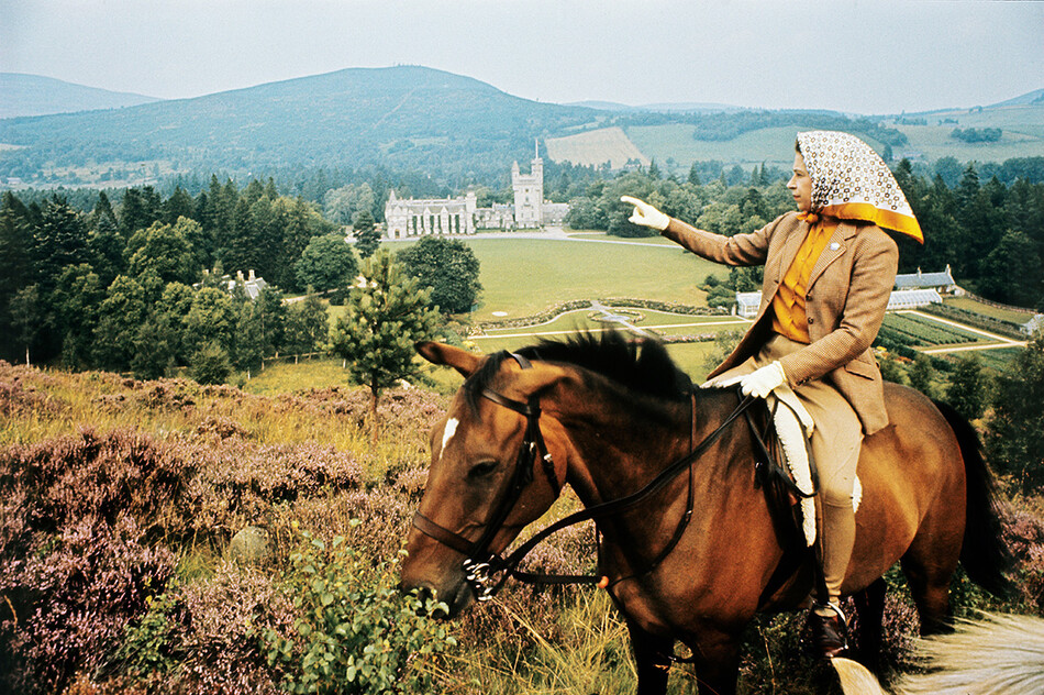 Королева Елизавета II верхом на лошади смотрит на замок Балморал в Шотландии 