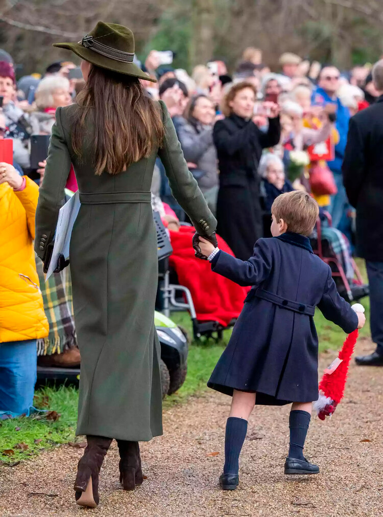 Принц Уэльский Луи тянет маму Кэтрин, принцессу Уэльскую размахивая подарком королевского фаната во время посещения рождественской службы в Сандрингемской церкви 25 декабря 2022 года в Сандрингеме, Норфолк