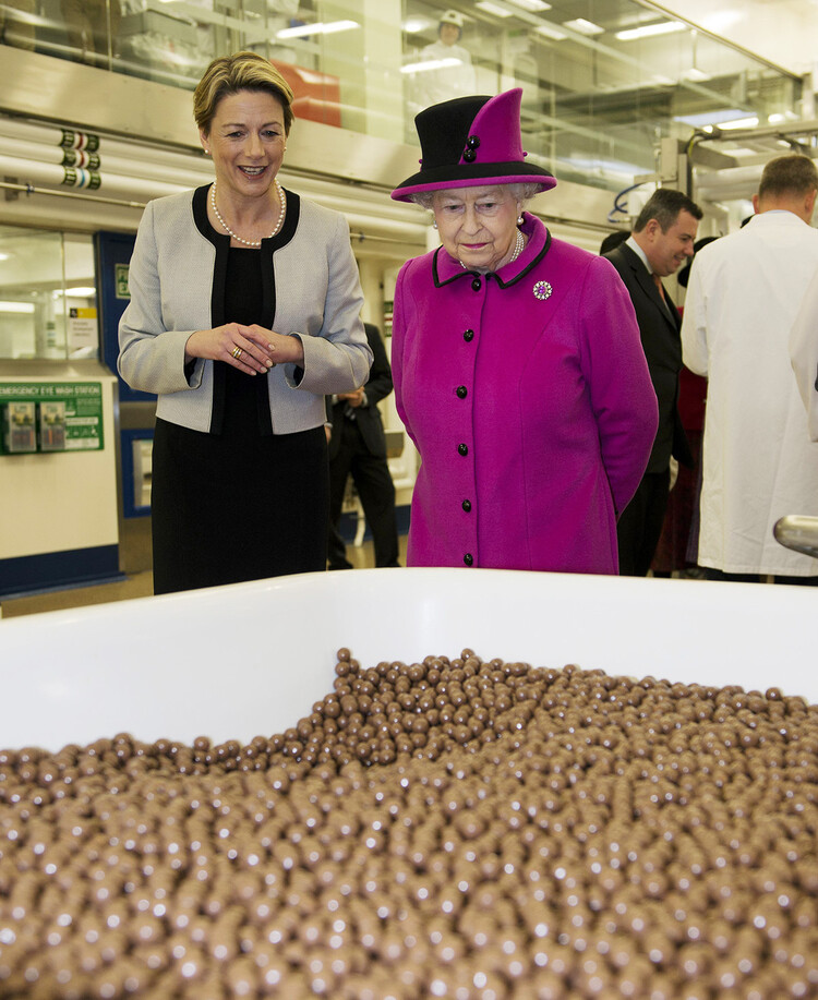 Королева Великобритании Елизавета II (справа) и Фиона Доусон (слева), президент Mars Chocolate UK, проходят мимо чана с шоколадными конфетами Maltesers во время посещения Mars Chocolate UK в Слау, южная Англия, 5 апреля 2013 года