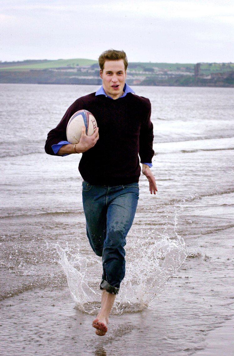 Принц Уильям смеется и бежит босиком по волнам, держа регби-футбол на пляже возле дома своего университета 29 мая 2003 г. в Сент-Эндрюс в Шотландии