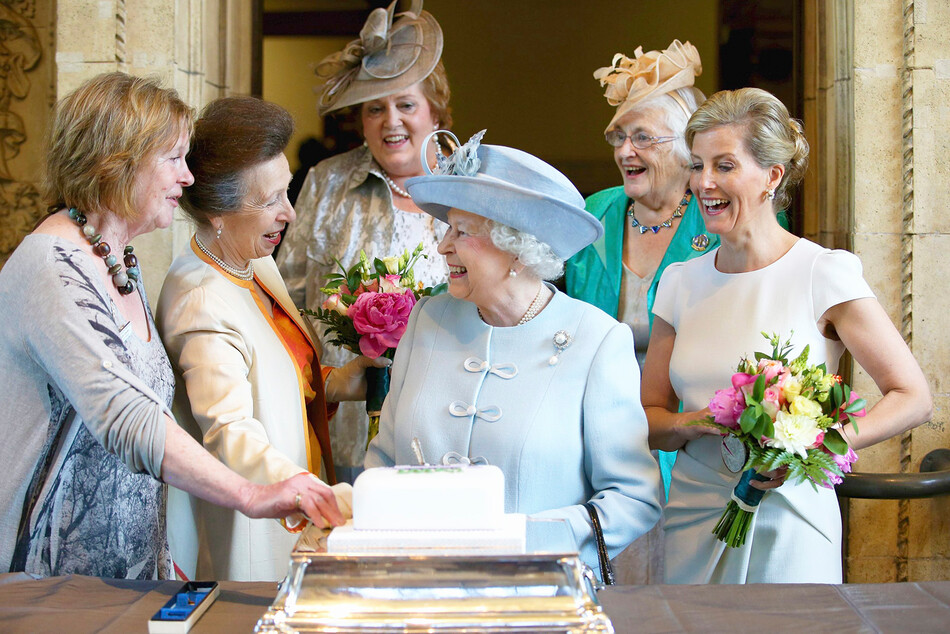 Софи, графиня Уэссекская и принцесса Анна, королевская принцесса наблюдают как королева Елизавета II разрезает торт, посвящённый 100-летию Женского института, на ежегодном столетнем собрании Национальной федерации женского института в Королевском Альберт-Холле 4 июня 2015 года в Лондоне, Англия