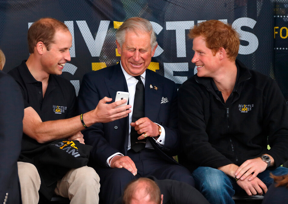 Принц Гарри с отцом, принцем Чарльзом и братом принцем Уильямом смотрят на мобильный телефон, на соревнованиях по лёгкой атлетики во время Игр непокоренных в Центре легкой атлетики Ли Вэлли 11 сентября 2014 года в Лондоне, Англия